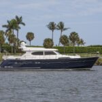 Elling E6 Highline yacht cruising past palm trees with an American flag waving, emphasizing its luxurious design in a tropical setting